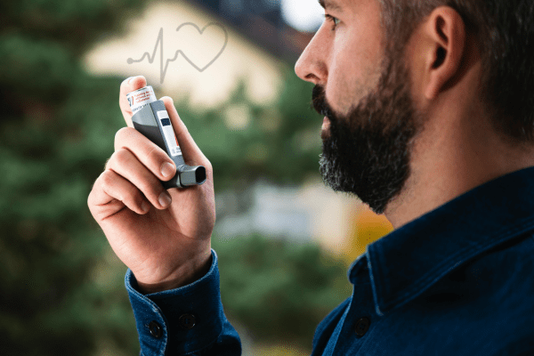 A man holding an asthma inhaler near his mouth, with a blurred outdoor background.
