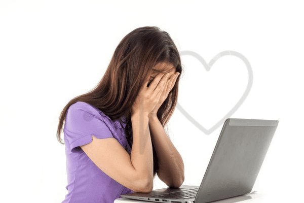 Woman sitting in front of a laptop with her face buried in hands, expressing stress or frustration.