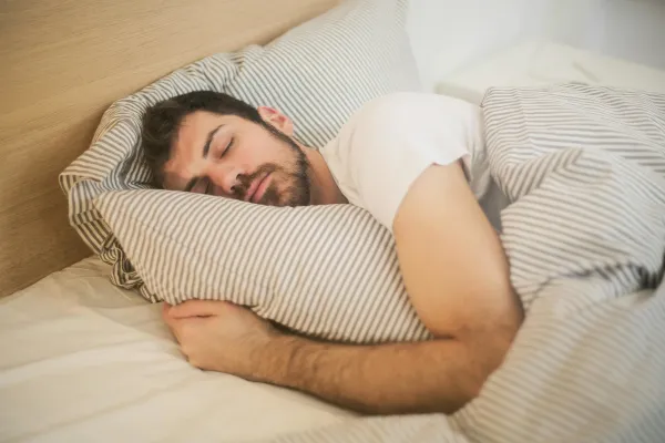 Man sleeping peacefully on a bed, representing deep sleep, relaxation, and stress recovery