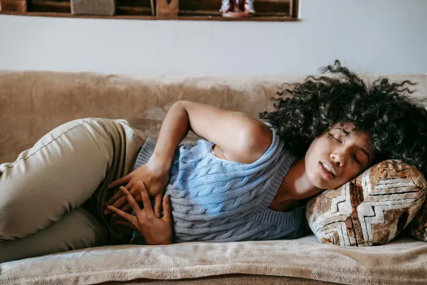 Woman lying on couch holding lower abdomen due to menstrual cramps